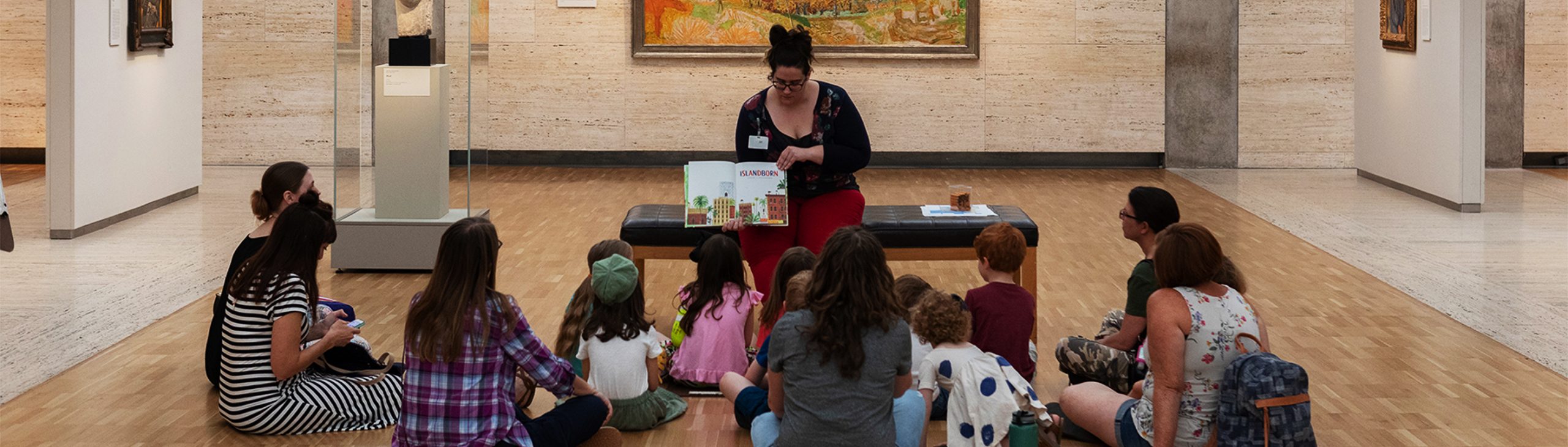 Teacher reads a book to students and parents in a museum